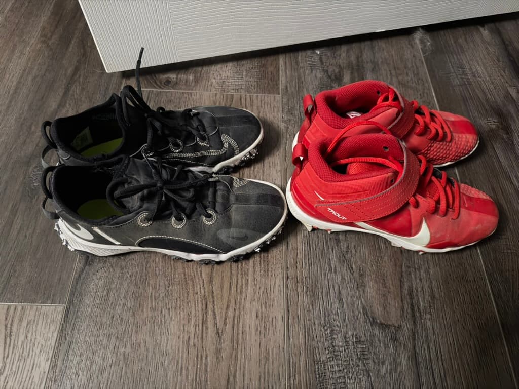 Black low-top cleats on the left beside red higher-cut cleats with ankle straps on the right.